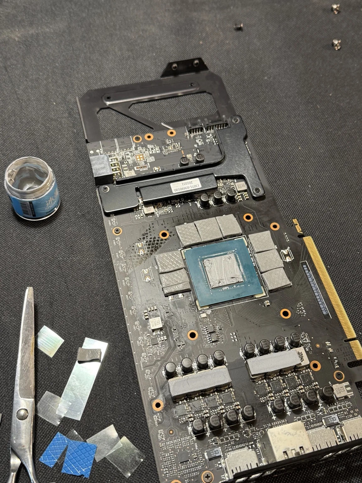 Placa de video desarmada en la mesa de trabajo de RAW, con pasta térmica y thermal pads durante el service